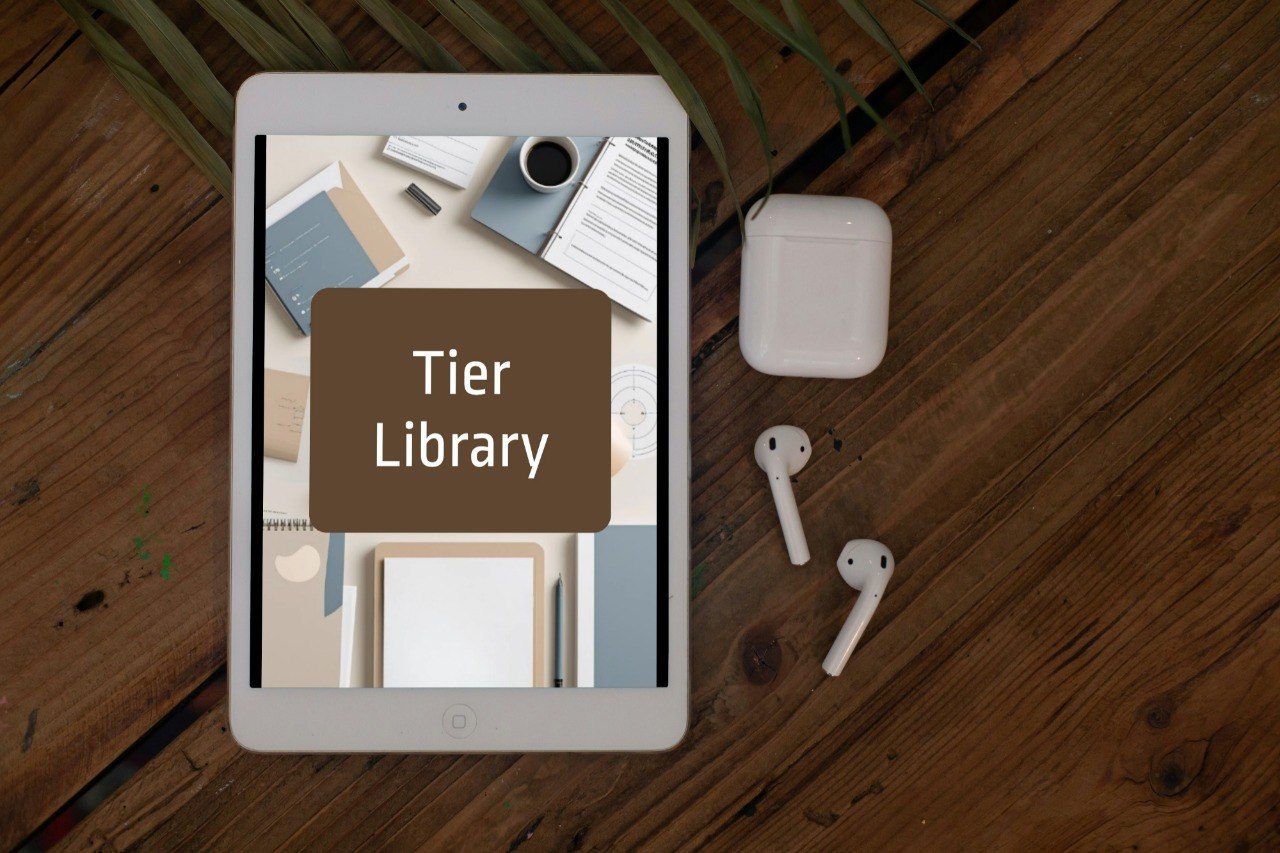 A tablet lying on a wooden tabletop, displaying a mock library cover with the text 'Tier Library' in a brown box. White wireless earbuds and a white charging case are placed beside the tablet, with a plant leaf visible in the upper background.